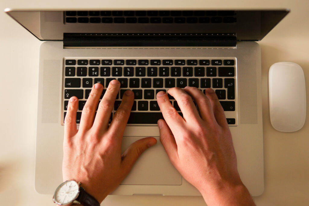Photo of male hands typing on laptop keyboard and using touchpad.
