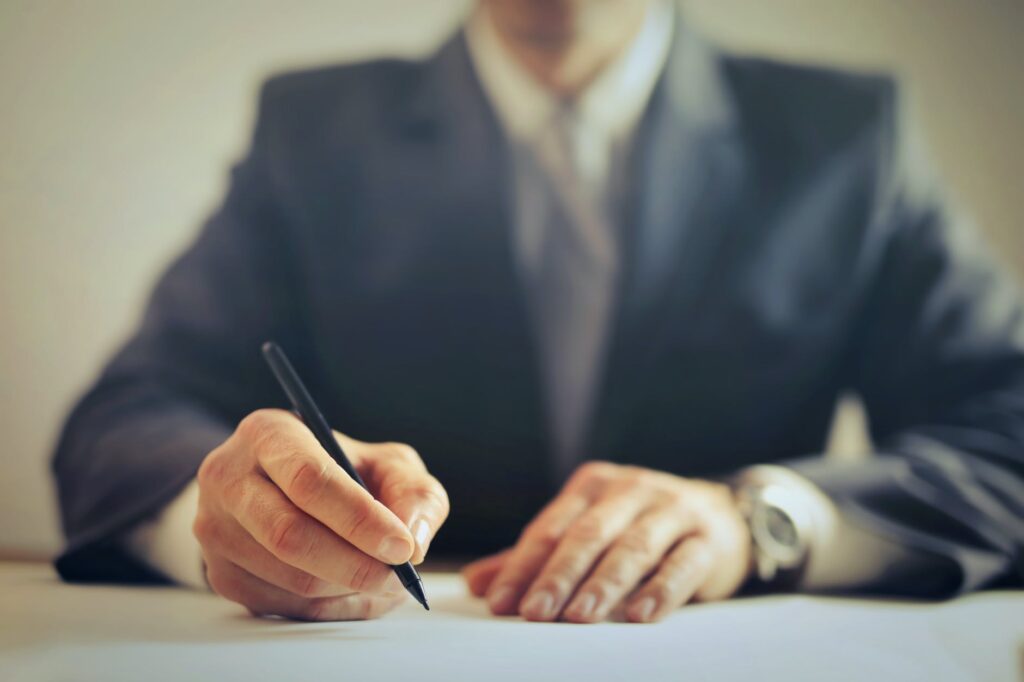 Businessman signing contract document on office desk, close up photo